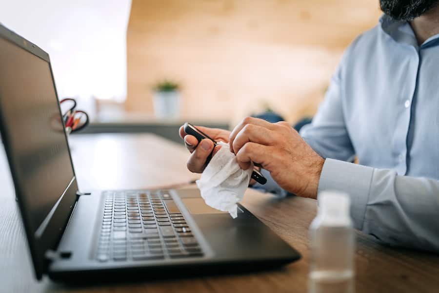 Mature man cleans and disinfects his smart phone in the office, using disposable wipes.