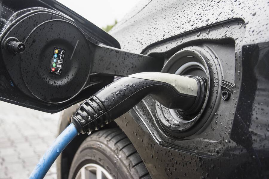 Symbolbild Elektroauto, der Akku wird im Freien an einem Regentag geladen, Ladestecker steckt im Fahrzeuganschluss E-Auto lädt im Regen *** Symbol image Electric car the Battery will in Free to a Rainy day loaded Charging plug lies in e Car loads in…