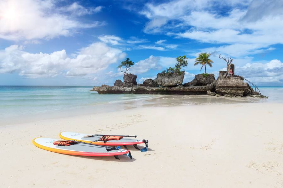 Strand auf der Insel Boracay, mit Blick auf eine kleinere Insel, zwei SUP-Boards am Ufer.