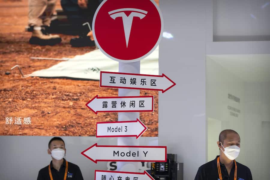 Staff members wearing face masks stand near a display at a booth for automaker Tesla at the China International Fair for Trade in Services (CIFTIS) in Beijing.