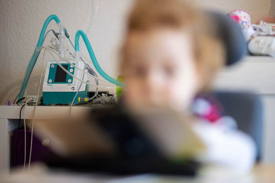 Ein Beatmungsgerät steht hinter einem Kind, das an spinaler Muskelatrophie (SMA) leidet.