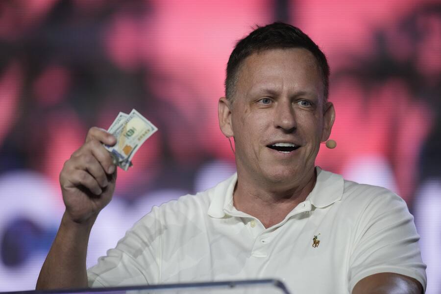 Peter Thiel, co-founder of PayPal and Palantir, offers a pair of hundred dollar bills to attendees during a keynote address at the Bitcoin Conference, April 7, 2022, in Miami Beach, Fla.