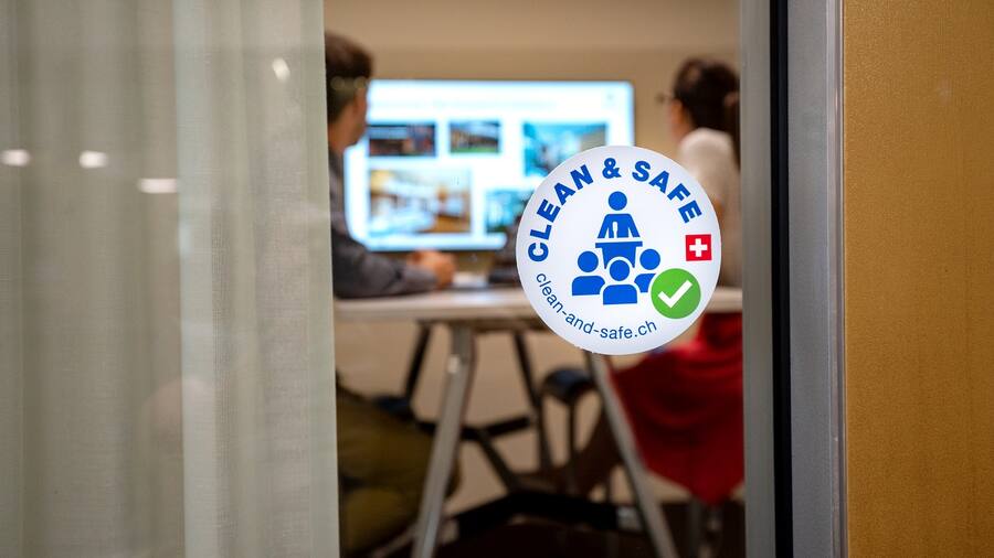 Clean and Safe Label Aufkleber von Business Events an der Scheibe eines Sitzungszimmer mit 2 arbeitenden Personen darin